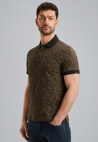 Brun polo shirt med et geometrisk mønster i guld, korte ærmer, sort krave, tre-knaps lukning og logo på brystet.