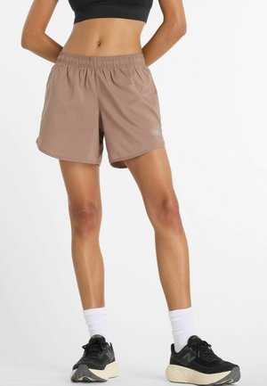Light brown athletic shorts with an elastic waistband. Features a small light blue logo. Worn with black shoes and white athletic socks.