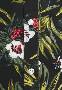 Kukkakuosinen lyhythihainen paita, jossa musta tausta, valkoisia ja punaisia kukkia, vihreitä lehtiä sekä valkoiset napit pliseerausalueella.