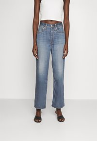 Jean taille haute bleu clair avec une coupe droite, comprenant cinq poches, des accents de couture dorée et une finition légèrement délavée.