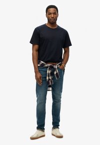 Marineblauwe katoenen t-shirt, lichtblauwe spijkerbroek, ruitjesoverhemd om de taille geknoopt, en beige sneakers met bruine rubberen zolen.