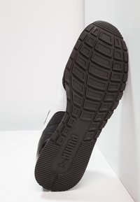 Zapatilla en blanco y negro con una suela de goma texturizada, que presenta un patrón de banda de rodadura pronunciado y una parte superior de tela suave.