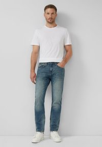 Jasnoniebieskie dżinsy o prostym kroju, zestawione z gładką białą koszulą z krótkim rękawem i białymi sneakersami, stojące na neutralnym tle.