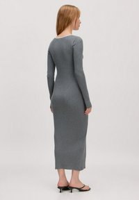 Enges, grau-farbenes Kleid mit langen Ärmeln aus geripptem Stoff und Rundhalsausschnitt. Das Kleid reicht bis zu den Knöcheln und wird mit schwarzen, hohen Sandalen kombiniert.