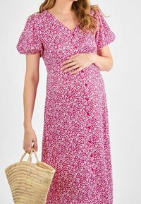 Kleid mit Puffärmeln, rosa floralem Muster, V-Ausschnitt und Knopfleiste, kombiniert mit einer geflochtenen Strohtasche. Geeignet für die Schwangerschaftsmode.