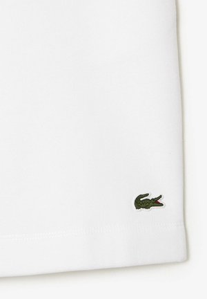 Weißer Stoff mit einem kleinen grünen, gestickten Krokodil-Logo nahe dem unteren Rand.