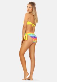 Zestaw bikini składający się z żółtego topu bandeau oraz majtek z wiązaniem po bokach, zdobiony wielokolorowym wzorem tie-dye, podkreślającym żywe kolory i gładką fakturę.