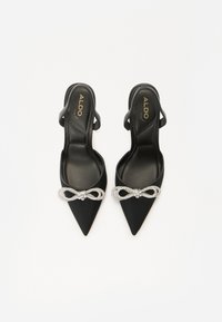 Talons hauts noires à dos ouvert avec des pointes, ornées d'un nœud en strass brillant sur le dessus. Texture lisse et semelle intérieure brillante.