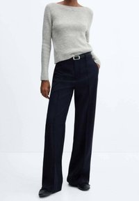 Hellgrau gerippter Strickpullover kombiniert mit dunkelblauen, gestreiften, weiten Hosenträgern und einem schwarzen Gürtel, mit glatter Textur und taillierter Passform.