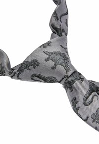 Cravate grise en tissu texturé avec un motif de dinosaures noirs, nouée. Le design présente différentes silhouettes de dinosaures.