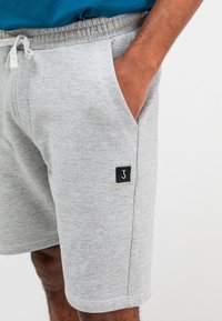 Grijze katoenen shorts met een elastische tailleband, zijzakken en een zwart label met een witte letter "J" op het linkerpoot.