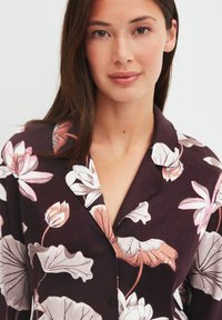 Bloemenblouse in donkerpaars met grote roze en witte bloemenprints, kraag en knoopsluiting. Zachte, gladde stof met een ontspannen ontwerp.