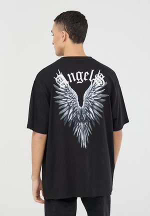 T-shirt nera in taglia oversize con una grande grafica di ali grigie e bianche sulla schiena, con la parola "Angels" sopra in caratteri in grassetto.
