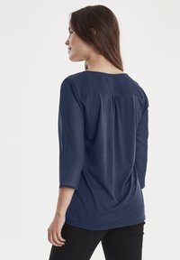Top blu navy a tre quarti con scollatura rotonda, dettagli plissettati sul retro e tessuto morbido e leggero.