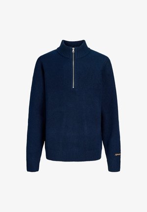 Zöld vízálló dzseki logóval, sötétkék kötött pulóver, fekete nadrág és szürke tornacipő. Kapucnival és elülső zsebekkel rendelkezik.