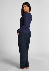 Marineblauwe longsleeve top gecombineerd met groen en marineblauwe geruite broek. De top is aansluitend, terwijl de broek een relaxte pasvorm en zakken heeft.