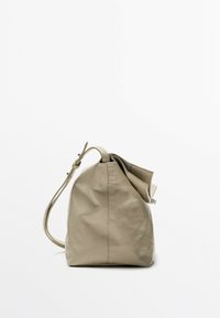 Beige leather handbag with a cylindrical shape, a drawstring closure, and a single shoulder strap. Smooth texture and minimal design.