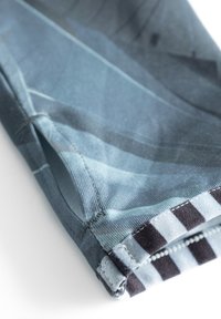 Blaue gemusterte Stoff mit einem geometrischen Design, versehen mit einem schwarz-weißen gestreiften Akzent am Saum und einer kleinen Öffnung an der Seite.