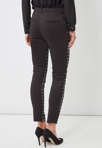 Pantalones ajustados negros con paneles laterales texturizados que presentan un patrón geométrico. Tejido suave, corte slim y dos bolsillos traseros.