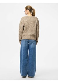 Beige gebreid sweater met een gestructureerd patroon, gecombineerd met hooggewaisted, wijde blauwe jeans. De outfit heeft een casual, ontspannen pasvorm.