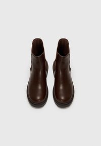 Botas de tobillo de cuero marrón con una textura suave, paneles laterales elásticos y una suela de goma baja, que presentan un diseño clásico de chelsea.