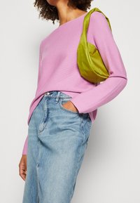 Pull en tricot rose avec un décolleté large, associé à une jupe en denim bleu clair taille mi-haute. Le mannequin porte un sac texturé vert.