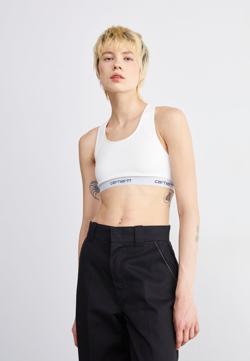Soutien-gorge de sport blanc à encolure dégagée et bande grise avec logo. Pantalon noir taille haute avec poches latérales et détails de couture subtils.