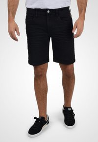Čierne denimové šortky so slim fit strihom, s prehnutým lemom, dizajnom s piatimi vreckami a zapínaním na gombík. Nosené s čiernymi teniskami.
