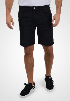 Črne denim kratke hlače slim fit kroja, s pripravljenim robom, petimi žepi in gumbom za zapiranje. Obute s črnimi teniskami.