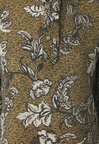 Bruin met bloempatronen, voorzien van een knoopsluiting, gemaakt van een textuurstof en met zwart-witte loofdetails.