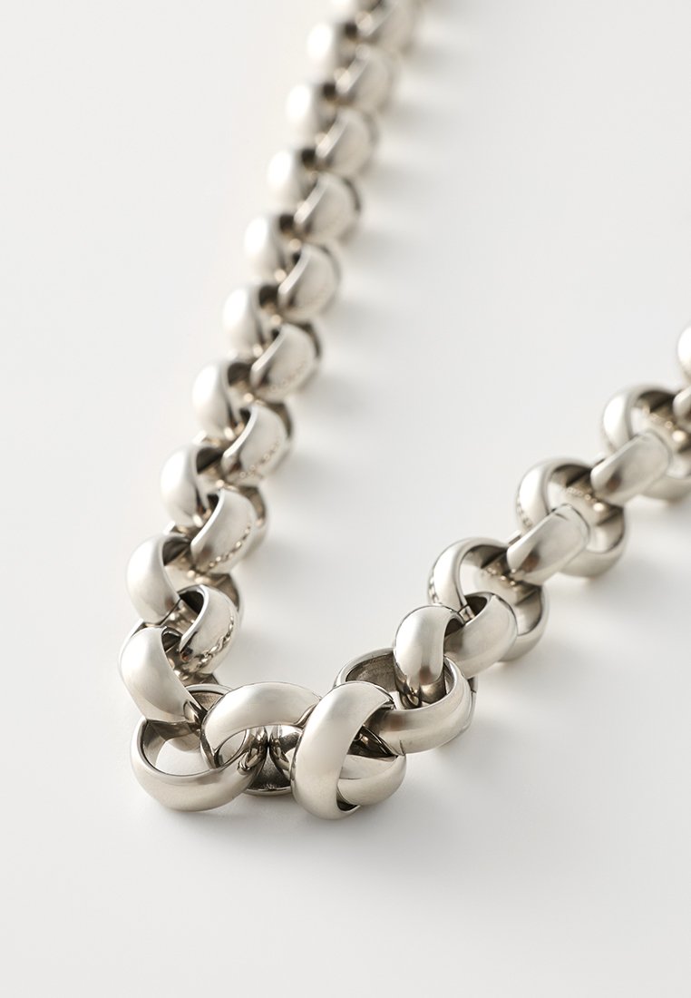 Collana in metallo con catena caratterizzata da anelli intrecciati con una finitura argentata lucida. Texture liscia e forma uniforme su tutta la lunghezza.