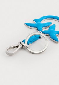 Chaveiro de pele azul com duas formas de pássaros, um clip de metal prateado e um anel circular. Superfície texturizada com acabamentos suaves.