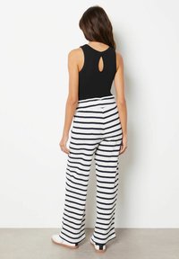 Černý bezrukávový top s výstřihem ve tvaru klíče; spárovaný s širokými pruhovanými kalhotami v bílé a námořnické modři. Hladká textura, ležérní design.