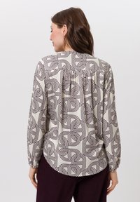 Langärmelig blouse in crèmekleur met een geometrisch bruin patroon, voorzien van een geplooide achterkant yoke en manchetten met knopen. Zachte, gladde stof.