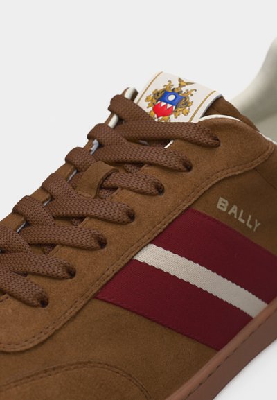 Καφέ σουέτ αθλητικό παπούτσι με καφέ κορδόνια, κόκκινη και λευκή πλαϊνή ρίγα, λογότυπο "BALLY" και έμβλημα μυτού.