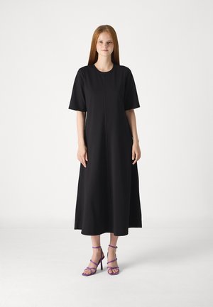 Black midi dress with short sleeves, round neckline, and subtle seam details; paired with purple strappy high-heeled sandals.