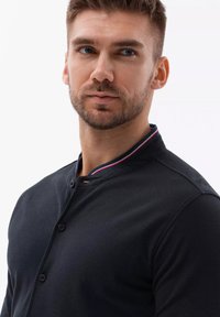 Zwarte button-up shirt met een korte kraag, voorzien van een rood en blauw streep. De stof lijkt glad met een subtiele textuur.