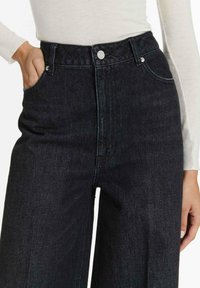 Hoge taille donkerdenim jeans hebben een recht gesneden ontwerp, twee voorkant vakken en een knoopsluiting met zilveren hardwareaccenten.