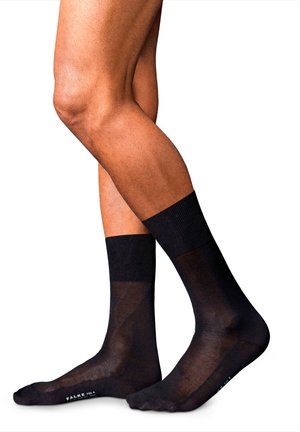 Calze nere trasparenti con polsino a coste, caratterizzate da una superficie liscia e un design a taglio basso, indossate su gambe di un modello su sfondo bianco.