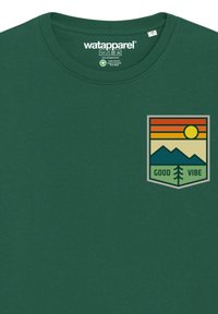 Groenen T-shirt van katoen met ronde hals. Kenmerkt een grafische patch met bergen, zon en de tekst "GOOD VIBE" in gedempte kleuren.