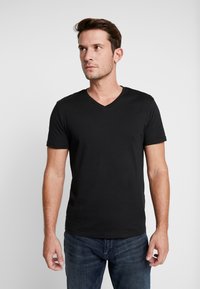 T-shirt noir à col en V en coton, avec des manches courtes et une coupe décontractée. Porté avec un jean bleu. Texture lisse, design minimal.