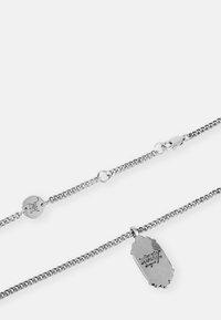 Colar de corrente prateada com elos texturizados e um pingente alongado. O pingente apresenta detalhes gravados e uma superfície lisa e brilhante.