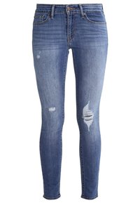 Jeans skinny de mezclilla en un tono azul claro con un acabado desgastado. Incluye bolsillos, cierre de botón y diversas áreas deshilachadas en las piernas.