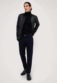 Chaqueta bomber de cuero negro, cuello de tortuga negro, pantalones azul oscuro, guantes negros y botas de tobillo; diseño elegante y aerodinámico.