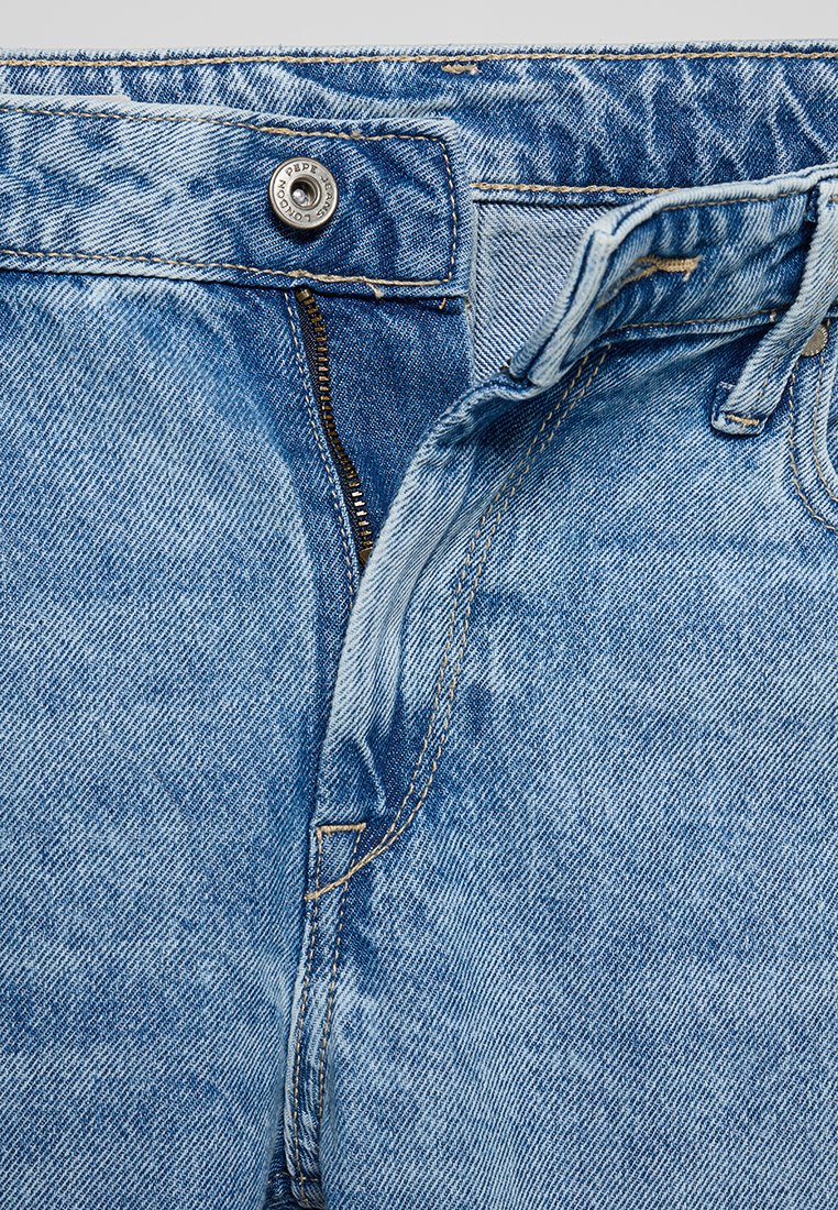 Jean en denim bleu clair avec fermeture éclair, bouton de fermeture et une texture légèrement délavée. Présente un design classique à cinq poches et des coutures de contraste.