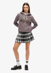 Paarse hoodie met geborduurde vogels en tekst, gecombineerd met een zwart-wit geruite mini-rok, zwarte schoenen en gestreepte witte sokken.