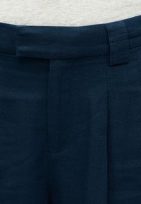 Ζώνη σκούρου ναυτικού μπλε παντελονιού με θηλιά ζώνης και κρυφό κούμπωμα, σε συνδυασμό με ανοιχτό γκρι ύφασμα πάνω από τη μέση.