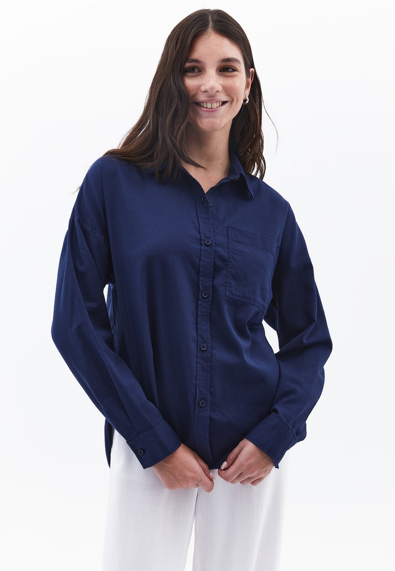 Camicia blu navy con bottoni realizzata in tessuto leggero. Presenta una tasca sul lato sinistro del petto e maniche leggermente oversized.
