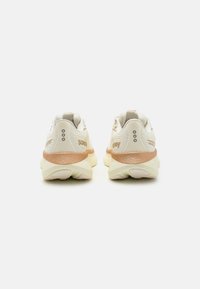 Baskets de sport beiges et crème avec des accents texturés, talon rembourré et trois trous de ventilation de chaque côté. Marque sur le talon.