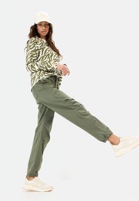 Groene camouflage lange mouw shirt gecombineerd met olijfgroene joggerpants en beige sneakers, met elastische manchetten en een comfortabele pasvorm.